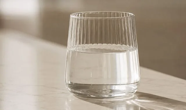 Žebrovaná sklenice čisté Kangen Water® na oslunněném pultu